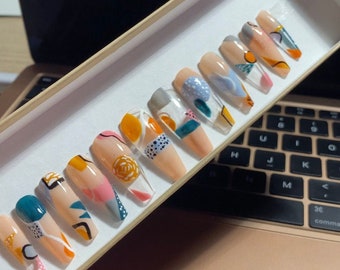 May include: A set of 10 false nails with an abstract design featuring geometric shapes, dots, and swirls in shades of blue, green, yellow, and white.