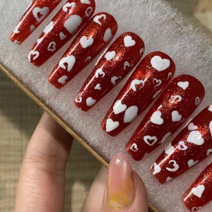 May include: Set of red glitter press-on nails with white heart designs.