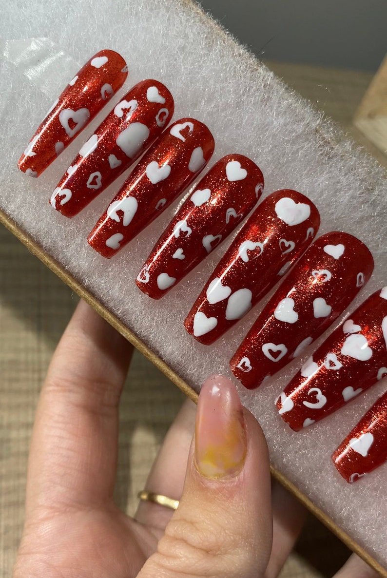 May include: Set of red glitter press-on nails with white heart designs.