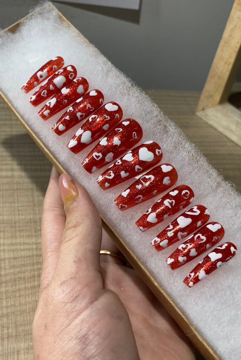 May include: Set of red and white press-on nails with a heart design. The nails are long and have a glossy finish.