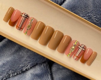 Peut inclure: Un ensemble de dix faux ongles avec un motif à carreaux brun et rose. Les ongles sont dans une boîte et sont prêts à être appliqués.