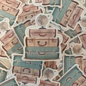 May include: A stack of three vintage suitcases with a globe on top. The suitcases are brown, beige, and teal. The globe is white with a brown map.