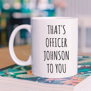 May include: White ceramic coffee mug with black text that reads "That's Officer Johnson to you".