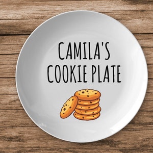 K&ouml;nnte beinhalten: Wei&szlig;e Keramikplatte mit schwarzem Text, der "Camila's Cookie Plate" lautet. Auf dem Teller ist ein Stapel Schokoladenkekse abgebildet.