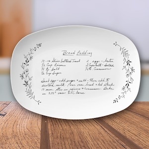 May include: White oval ceramic serving platter with a handwritten recipe for bread pudding. The recipe includes ingredients like buttered toast, raisins, salt, sugar, eggs, milk, and cinnamon. The platter is decorated with a floral border.