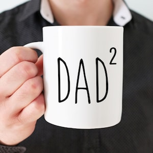 Op de afbeelding: Een witte keramische mok met een zwarte inscriptie die "DAD²" luidt.