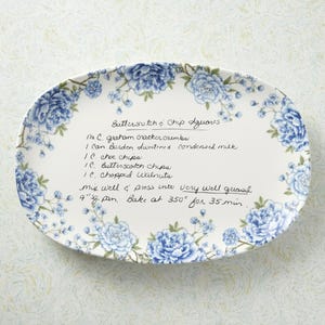 May include: An oval serving platter with a white background and a blue floral border. The platter has handwritten text that appears to be a recipe for Butterscotch & Chip Squares.