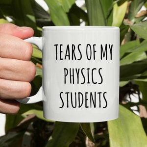 May include: White ceramic coffee mug with black text that reads "Tears of my Physics Students".
