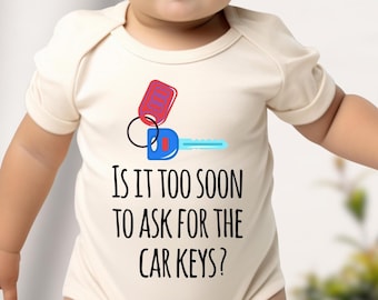 Puede incluir: Un body de bebé color crema con el texto "IS IT TOO SOON TO ASK FOR THE CAR KEYS?" y un gráfico de llaves de coche. El gráfico de la llave es rojo, azul y azul claro.