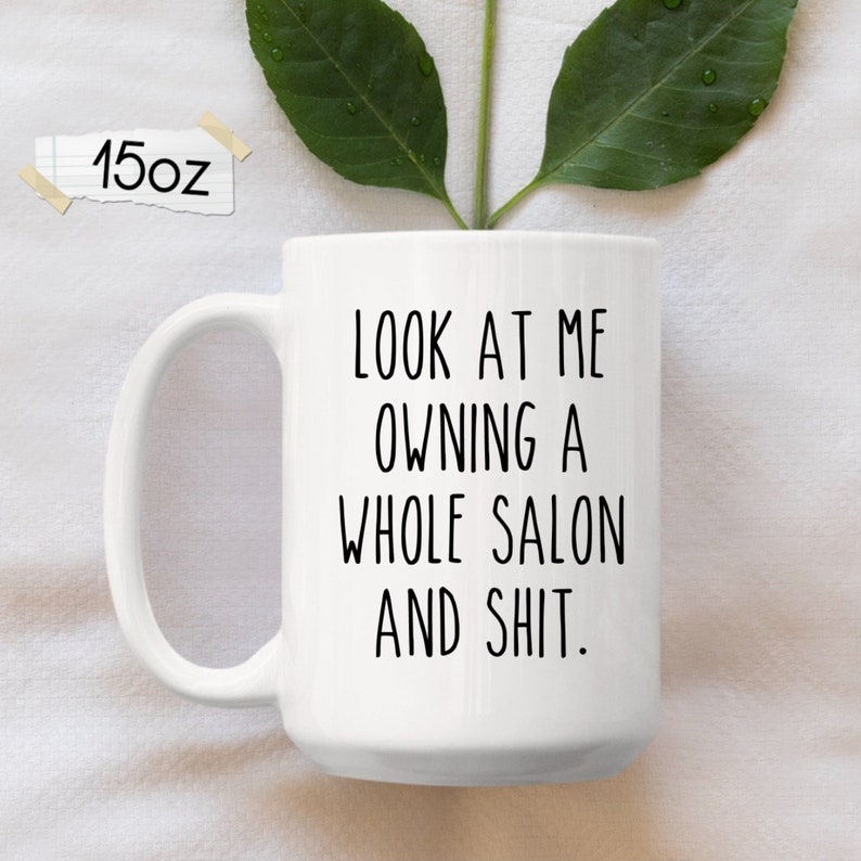 Może przedstawiać: Biały ceramiczny kubek do kawy z czarnym napisem "LOOK AT ME OWNING A WHOLE SALON AND SHIT."