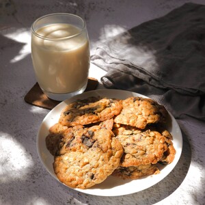 K&ouml;nnte beinhalten: Ein wei&szlig;er Teller mit einem Stapel Schokoladen-Chip-Cookies, einige mit wei&szlig;en Schokoladenst&uuml;ckchen, auf einer wei&szlig;en Oberfl&auml;che mit einem Glas Milch und einer grauen Stoffserviette.