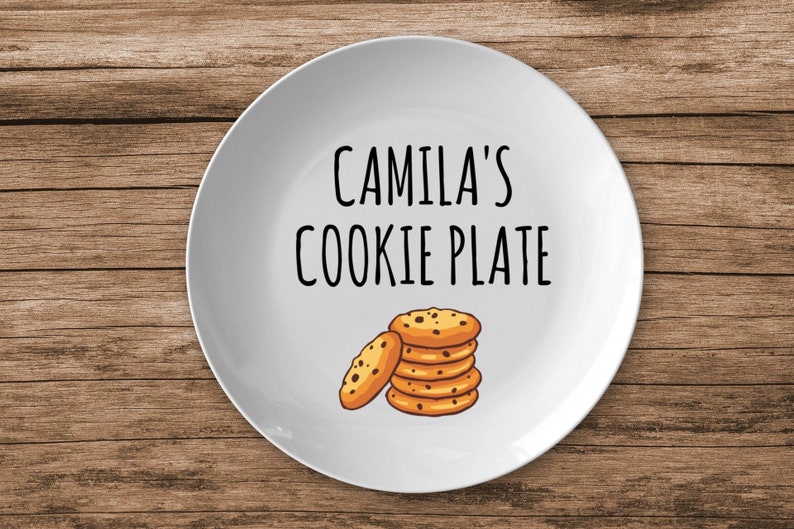 K&ouml;nnte beinhalten: Wei&szlig;e Keramikplatte mit schwarzem Text, der "Camila's Cookie Plate" lautet. Auf dem Teller ist ein Stapel Schokoladenkekse abgebildet.