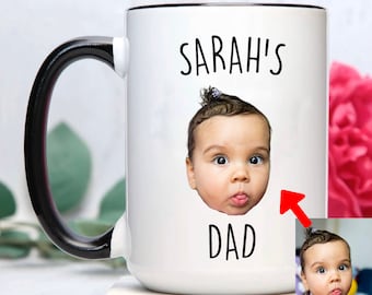 Op de afbeelding: Een witte keramische mok met een zwart handvat. De mok heeft een foto van een baby met de tekst "SARAH'S DAD" erop gedrukt.
