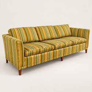 May include: A three-cushion sofa upholstered in a vertical striped fabric featuring shades of olive green, mustard yellow, and soft peach. The piece includes three back cushions, three seat cushions, and tapered wooden legs at the base.