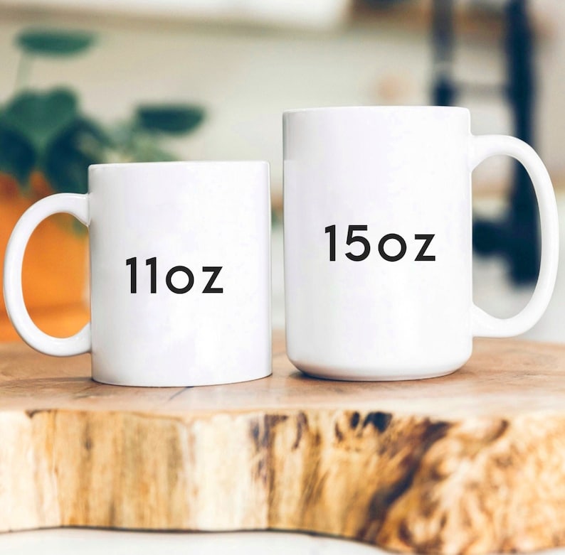 May include: Two white ceramic mugs with black text. The smaller mug says "11oz" and the larger mug says "15oz".