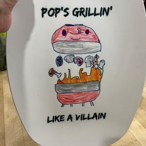 May include: A white oval platter featuring a hand-drawn illustration of a red grill with orange flames. The drawing includes various food items and the black text "POP'S GRILLIN'" at the top and "LIKE A VILLAIN" at the bottom of the platter.
