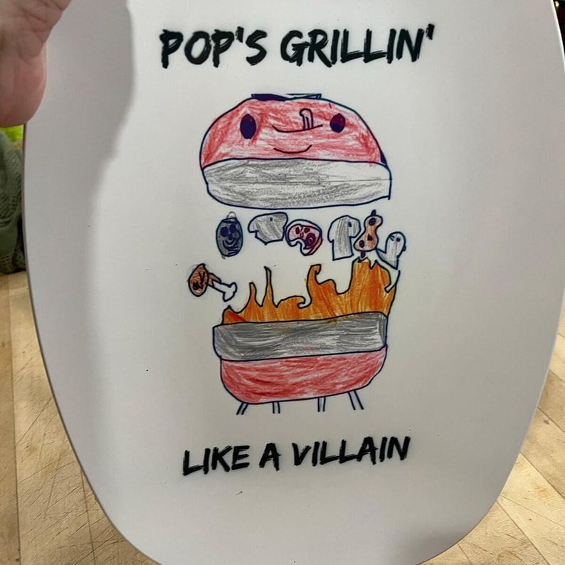May include: A white oval platter featuring a hand-drawn illustration of a red grill with orange flames. The drawing includes various food items and the black text "POP'S GRILLIN'" at the top and "LIKE A VILLAIN" at the bottom of the platter.