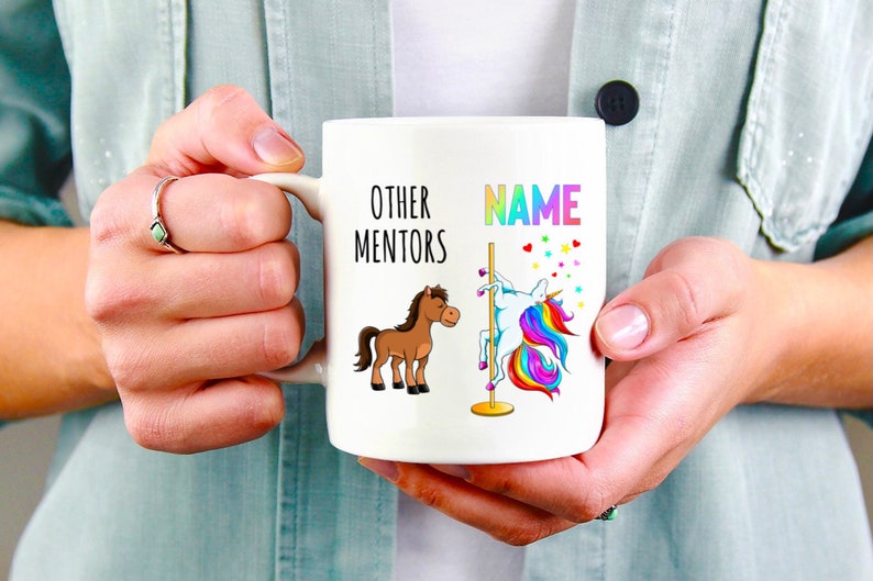 May include: White ceramic coffee mug featuring a brown horse and a rainbow unicorn on a pole. The text on the mug reads "Other Mentors" and "NAME".