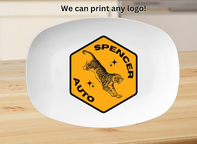 May include: A white oval plate featuring a central yellow hexagon graphic with a black border. The graphic displays a leaping tiger, two four-pointed stars, and the black text "SPENCER AUTO". Above the plate, the text "We can print any logo!" appears.