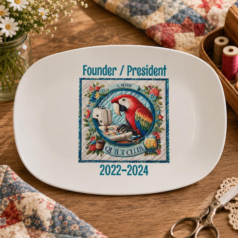 May include: A white oval ceramic plate featuring a central graphic of a colorful parrot sitting at a sewing machine. The text reads Founder / President and 2022-2024, with L MHH QUILT CLUB printed within a circular blue border surrounded by floral motifs.