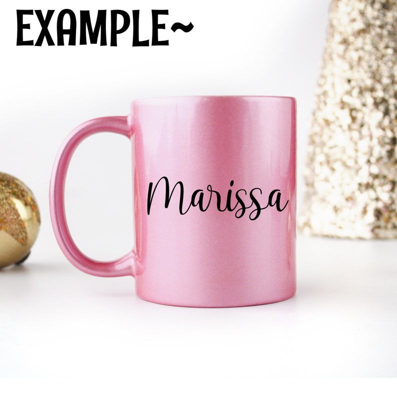 Puede incluir: Una taza de cer&aacute;mica rosa con el nombre "Marissa" escrito en cursiva negra en la parte delantera.