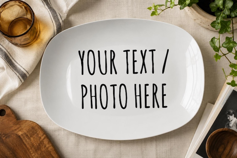 May include: A white oval ceramic serving platter featuring the black printed text "YOUR TEXT / PHOTO HERE" centered on the surface. The platter has a smooth, glossy finish and rounded edges, providing a clean and neutral base for custom designs.