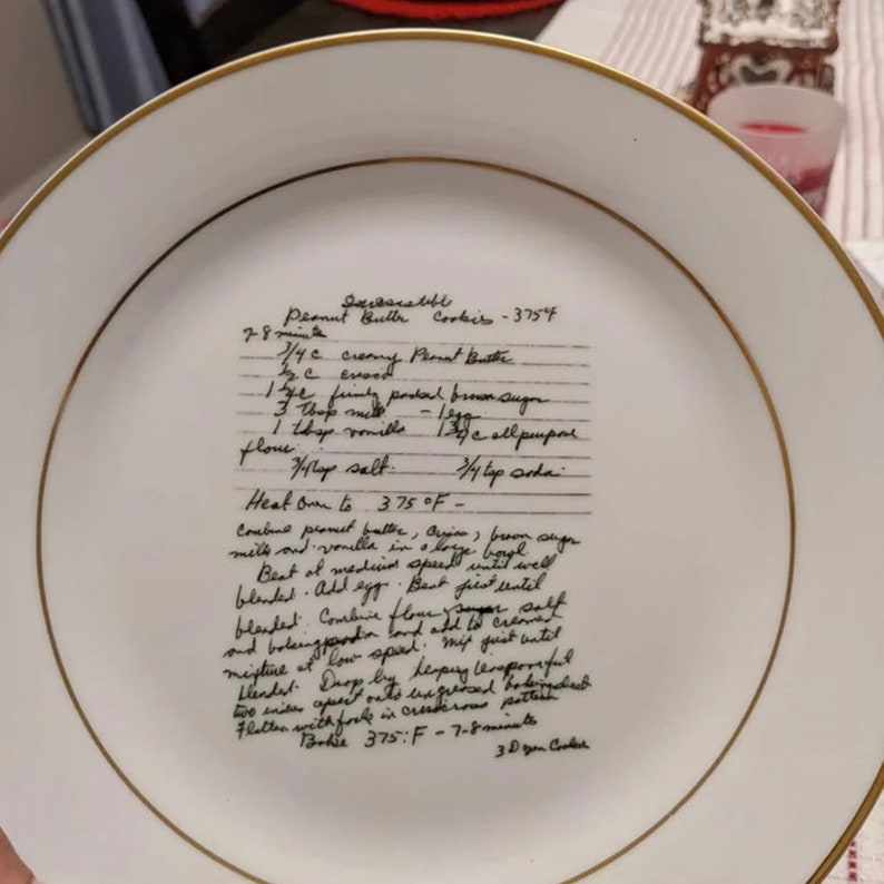 May include: A white ceramic plate with a handwritten peanut butter cookie recipe. The recipe includes ingredients like creamy peanut butter, brown sugar, all-purpose flour, salt, and baking soda. The instructions include beating the ingredients together, adding an egg, and baking the cookies at 375 degrees Fahrenheit for 7-8 minutes.