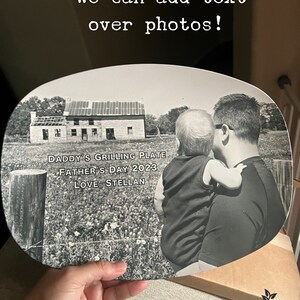 May include: An oval-shaped plate featuring a black and white photograph of a person holding a child in front of a house. The text on the plate reads: DADDY'S GRILLING PLATE, FATHER'S DAY 2023, LOVE, STELLAN. The top of the image includes the text: We can add text over photos!