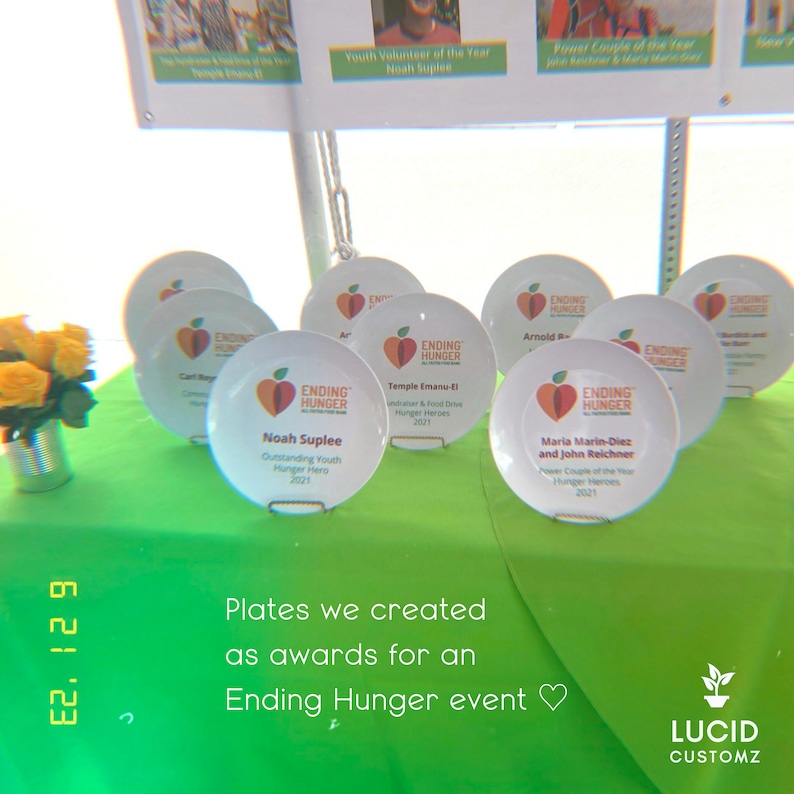May include: A collection of white ceramic plates with a red apple logo and the text "Ending Hunger" on each plate. The plates are arranged on a green tablecloth with the text "Plates we created as awards for an Ending Hunger event" below them.
