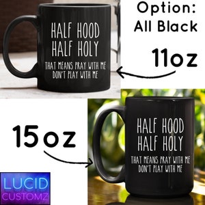 K&ouml;nnte beinhalten: Schwarze Keramik-Kaffeetasse mit wei&szlig;em Text, der "Half Hood Half Holy That Means Pray With Me Don't Play With Me" lautet. Die Tasse ist in den Gr&ouml;&szlig;en 11 oz und 15 oz erh&auml;ltlich.