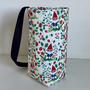 May include: A white fabric tote bag with a black strap. The bag has a repeating pattern of gnomes, strawberries, and flowers.