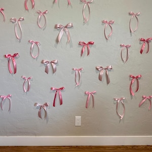May include: A wall decorated with pink satin bows of various sizes and shades. The bows are arranged in a random pattern, creating a whimsical and festive atmosphere.