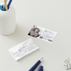 K&ouml;nnte beinhalten: Eine wei&szlig;e Visitenkarte mit einem Foto einer Frau und dem Text "Your Name" und "Real Estate Professional". Die Karte enth&auml;lt auch ein Logo, Kontaktinformationen, einen QR-Code und den Text "exp" in Schwarz.