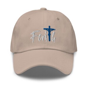 May include: A beige baseball cap with an embroidered design of a cross with a figure on it and the word "Faith" in white lettering.
