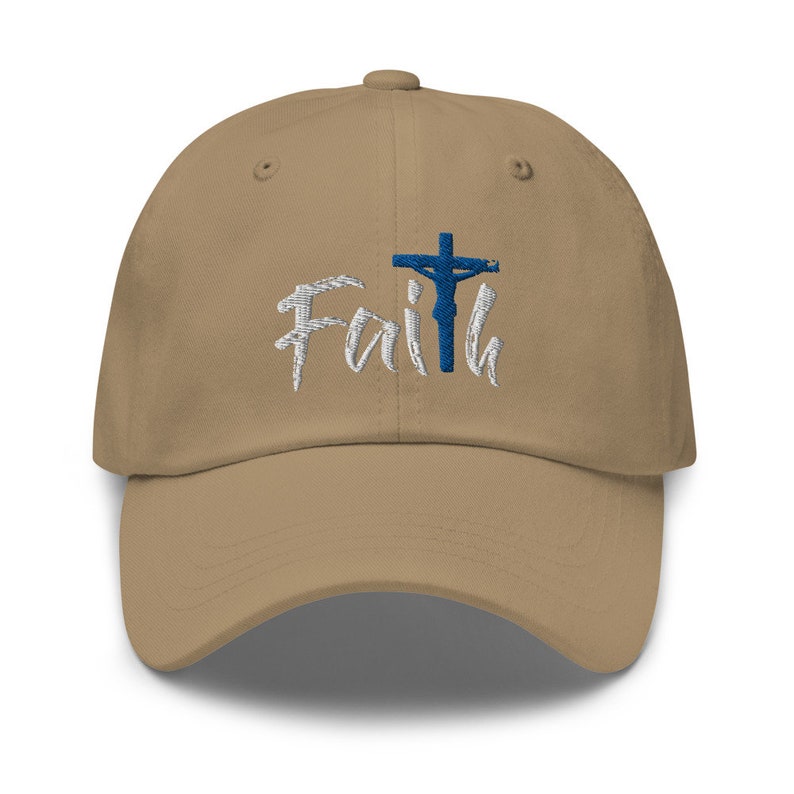 May include: A tan baseball cap with an embroidered white design that says "Faith" with a blue cross and a blue figure of Jesus on the cross.