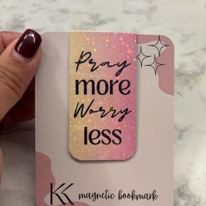 May include: A magnetic bookmark with a pink and yellow gradient design. The bookmark features the text "Pray more Worry less" in black script. The bottom of the bookmark has the text "magnetic bookmark".