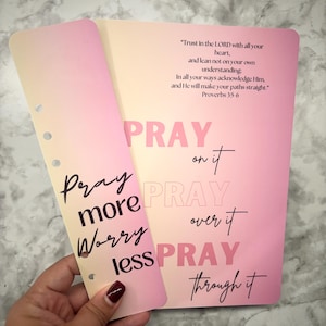May include: Two planner inserts with a pink and yellow gradient. One insert reads "Pray more, Worry less" in black script. The other insert has the words "PRAY" in pink and "Pray on it, Pray over it, Pray through it" in black script. The text "Trust in the LORD..." is also visible.