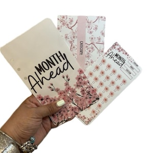 May include: Three white planner inserts featuring pink cherry blossom patterns. The largest insert displays the text Month Ahead in black script. A second insert features a vertical Category label, while the third includes Month Ahead text.