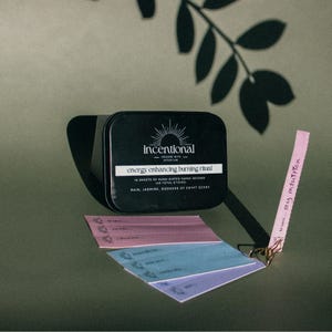 May include: A black tin box with the words "incentional" and "energy enhancing burning ritual" printed on it. The box contains 16 sheets of hand-dipped paper incense with a rain, jasmine, goddess of Egypt scent.