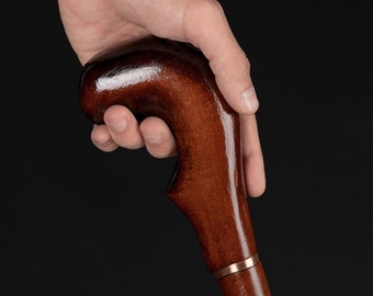 May include: A close-up of a wooden walking stick with a brown, curved handle. The handle has a gold band around it.