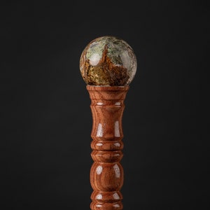 Puede incluir: Un bastón de madera con una parte superior decorativa hecha de una esfera con un patrón verde, marrón y blanco.
