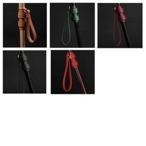 May include: Five leather wrist straps in different colors, each attached to a wooden walking stick. The straps are brown, green, red, black, and burgundy.