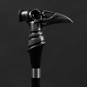 Pode incluir: Uma bengala preta com uma pega detalhada em forma de cabe&ccedil;a de corvo. A pega &eacute; esculpida com um design em espiral texturizado.