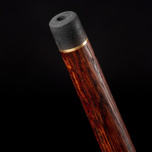 Puede incluir: Primer plano de la parte superior de un bast&oacute;n de madera con una punta de goma negra y una banda dorada.