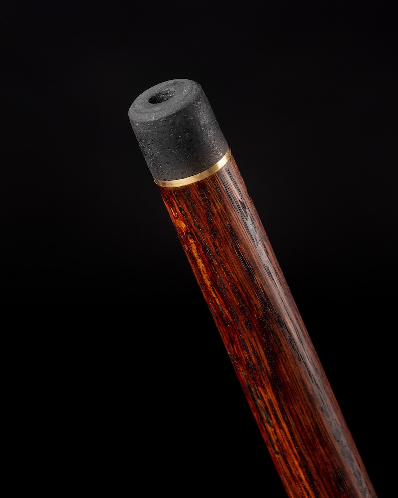 Puede incluir: Primer plano de la parte superior de un bast&oacute;n de madera con una punta de goma negra y una banda dorada.