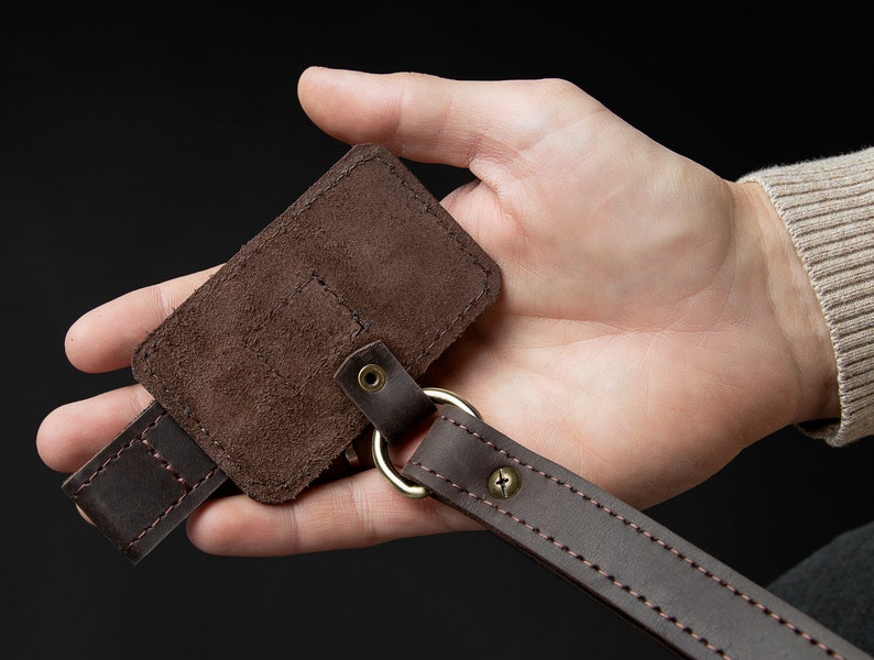 May include: A brown leather key chain with a suede key holder. The key holder has a stitched flap and a metal ring.