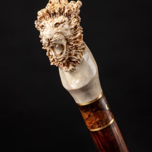 Puede incluir: Un bast&oacute;n con un mango tallado en forma de cabeza de le&oacute;n. El mango est&aacute; hecho de hueso y el eje est&aacute; hecho de madera oscura con una banda dorada.