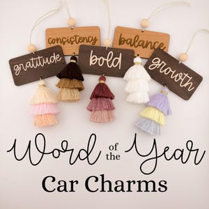 May include: Word of the Year car charms with wooden tags and tassel accents. The tags feature the words "gratitude", "consistency", "bold", "balance", "growth".
