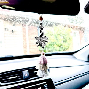 May include: A black and white lighthouse with flowers hanging from a rearview mirror in a car. The lighthouse is surrounded by a white tassel.