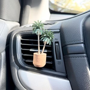 May include: A miniature palm tree air freshener. The small, green palm trees are set in a cork pot and are designed to clip into a car's air vent. The air freshener is a decorative car accessory.